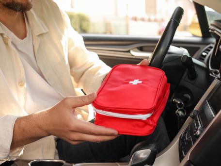 Mann sitzt im Auto und hält einen Autoverbandskasten in den Händen