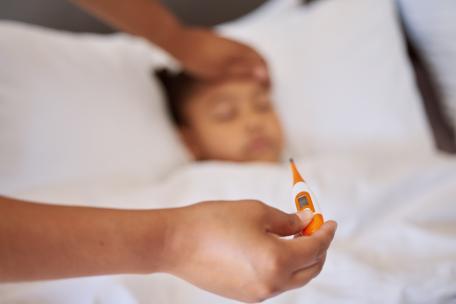 Mädchen liegt im Bett und bekommt Fieber gemessen